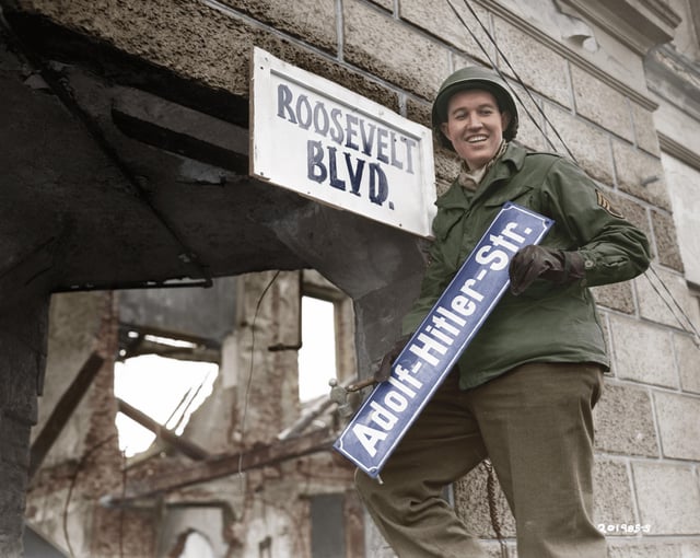 Staff Sergeant George A. Kaufman replacing a road sign from 'Adolf Hitler Str.' to 'Roosevelt Blvd.' in the German town of Krefeld shortly after its capture by Allied forces. The street was later renamed to Rheinstraße. (1945) [2505×2000]